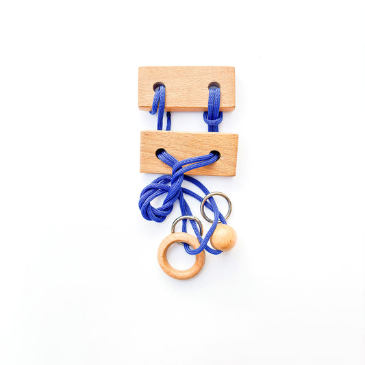Wooden puzzle with blue rope and rings on a white background. This classic brain teaser toy challenges players to manipulate the rope to separate the rings from the puzzle