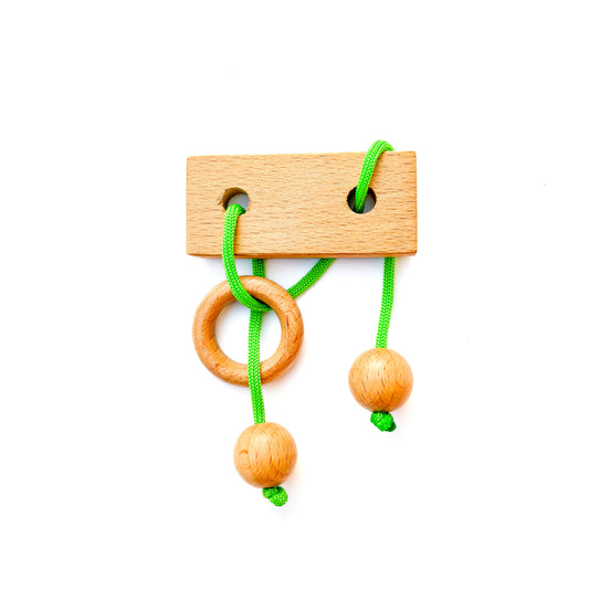 Wooden string puzzle with green thread on a white background. This classic brain teaser toy challenges players to manipulate the loop of green thread to disentangle the wooden pieces. 